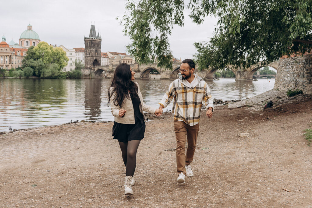 Couple celebrating engagement with Charles Bridge behind them in Prague