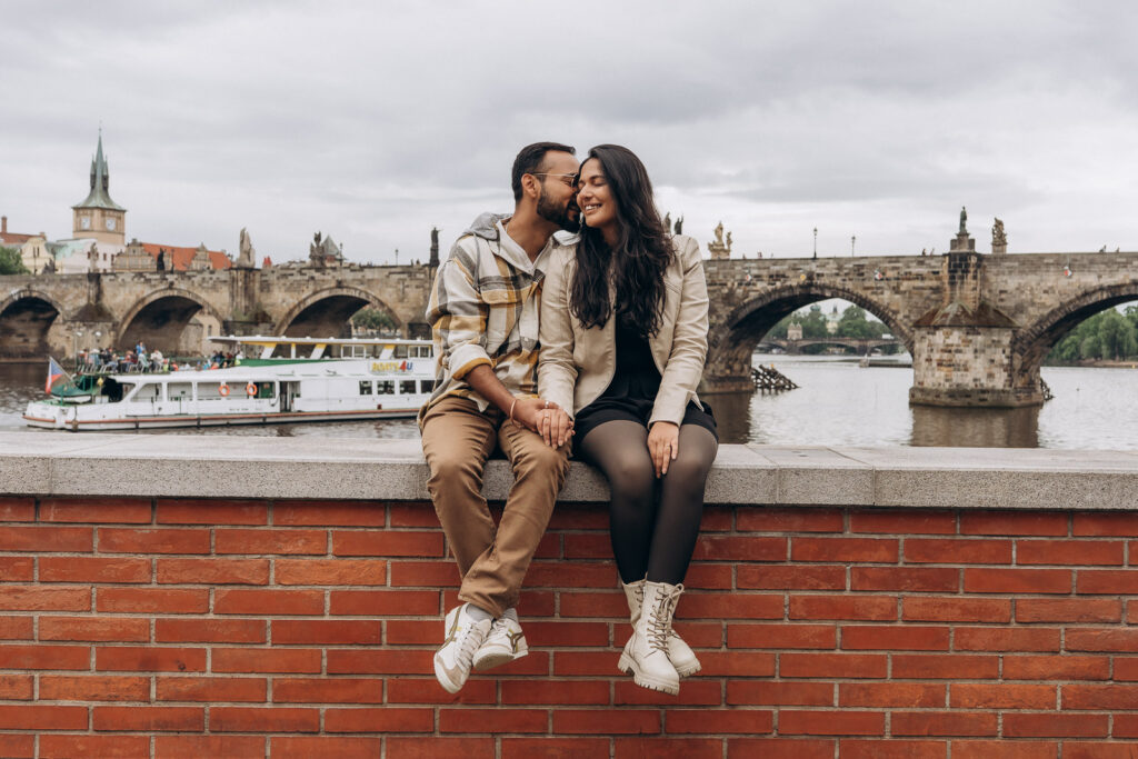 Couple celebrating engagement with Charles Bridge in Prague behind them