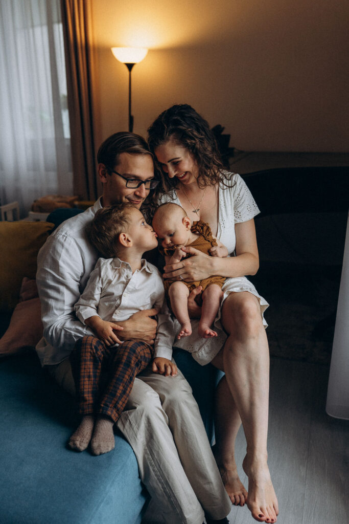 Parents holding newborn girl and toddler boy during home photoshoot in Prague