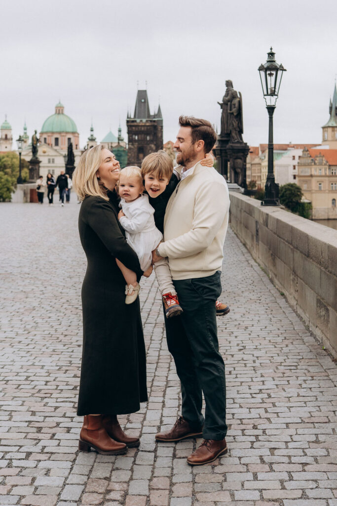 Parents holding children during family photoshoot on Charles Bridge, Prague