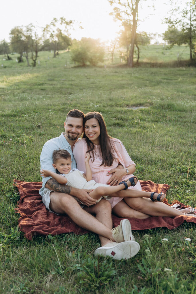 Expecting mother and dad with toddler son during golden hour photoshoot at Břevnov Monastery