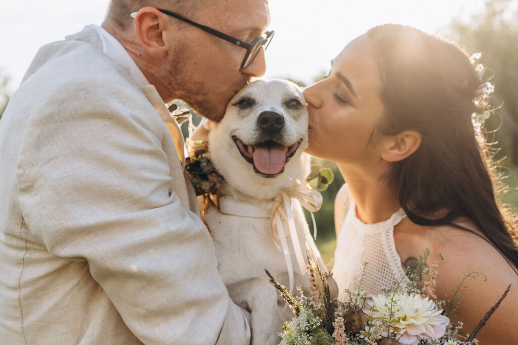 Bride and groom kissing their dog during laid-back outdoor wedding near Prague