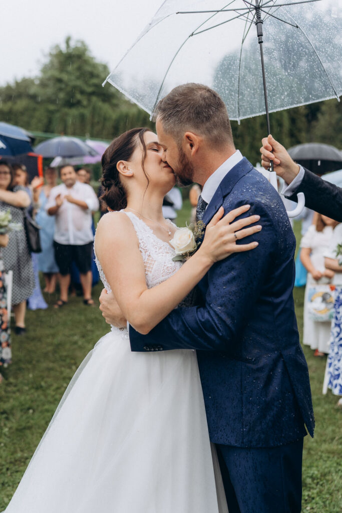 Bride and groom sharing first kiss during rainy wedding near Prague