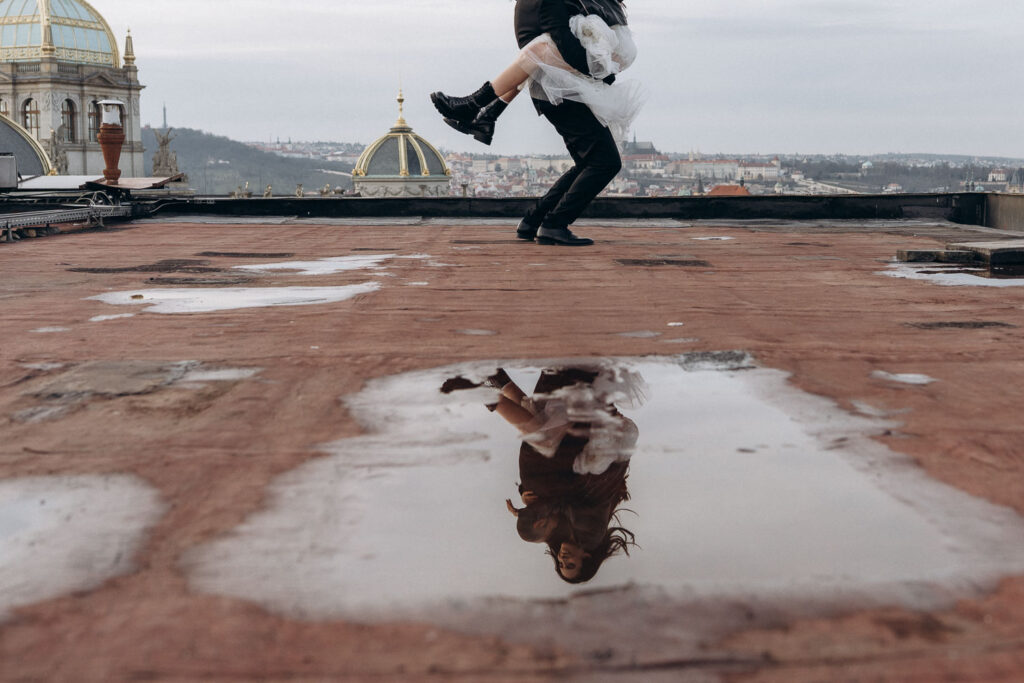 Bride and groom reflection on rooftop during editorial wedding photos with Prague museum view