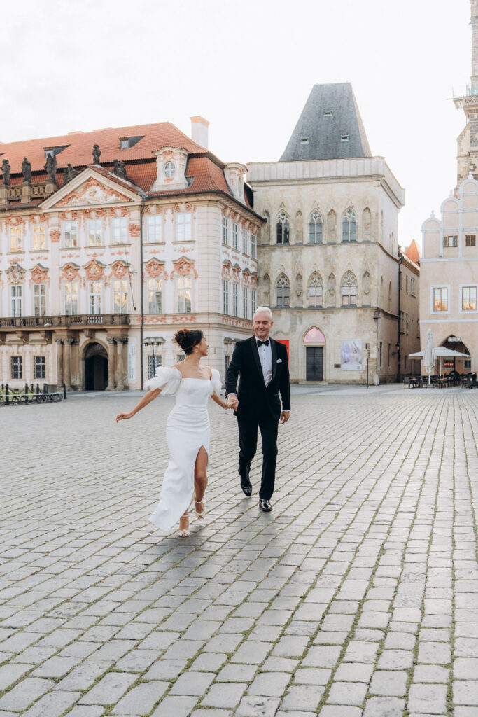 Bride and groom walking through Old Town Square at sunrise