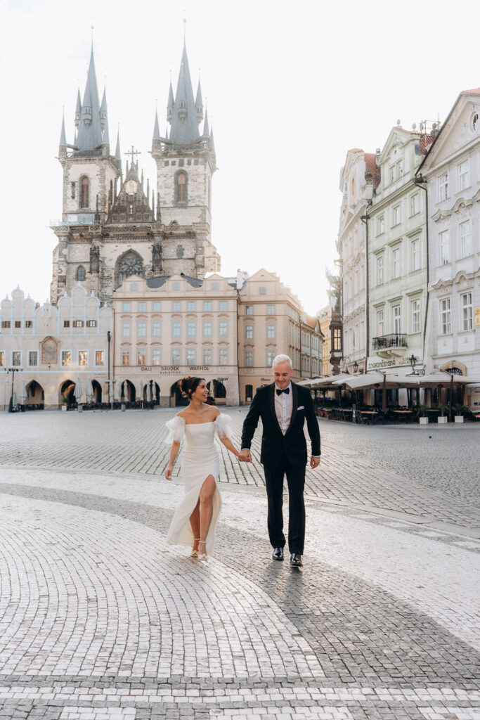 Bride and groom walking through Old Town Square at sunrise