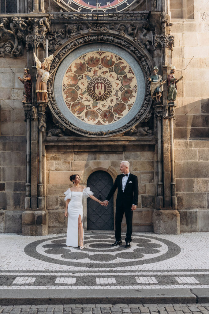 Bride and groom standing together by Astronomical Clock at sunrise in Prague